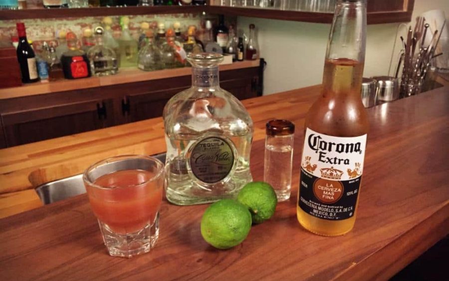 Sangrita cocktail with ingredients: tequila, limes, and Corona on a bar