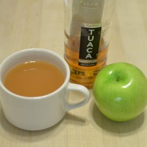 Hot Apple Pie cocktail in a mug with a green apple and bottle of alcohol