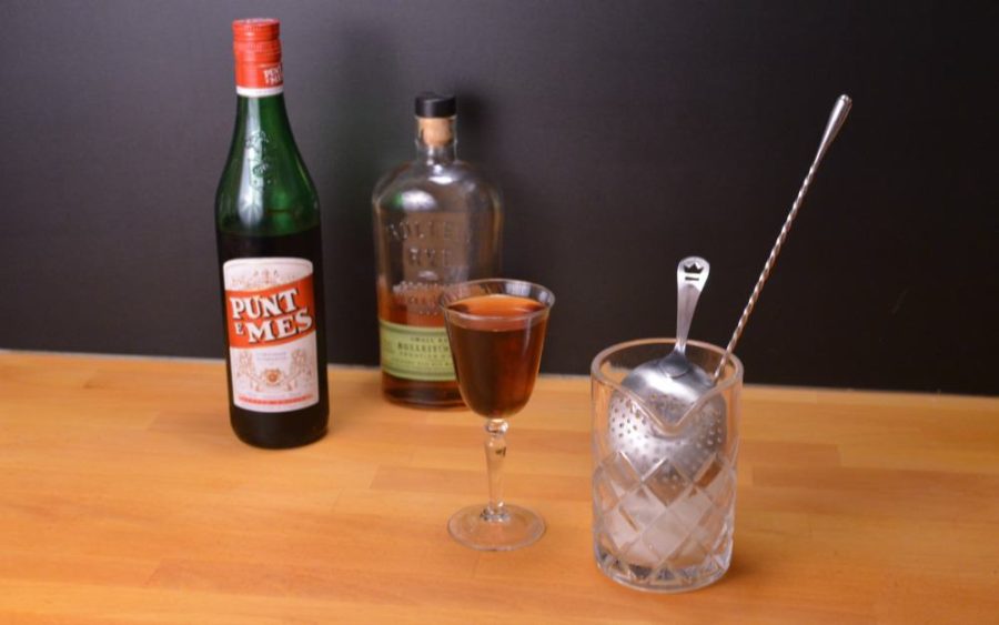 Red Hook cocktail next to a bottle of whiskey and a mixing glass
