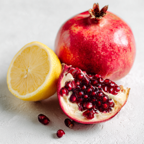 a pomegranate cut open to show the pomegranate seeds, next to a lemon half