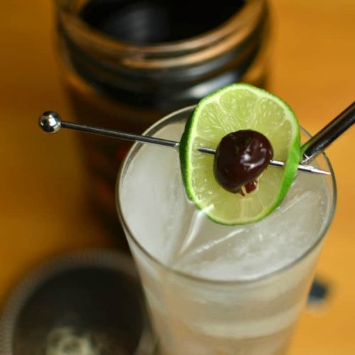 Rum and lime Collins with a lime wheel and cocktail cherry, in a tall glass