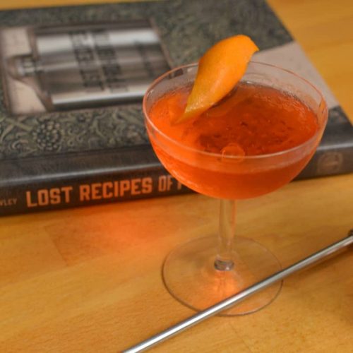 Lucien Gaudien cocktail, an orange-red cocktail with orange peel in a coupe glass