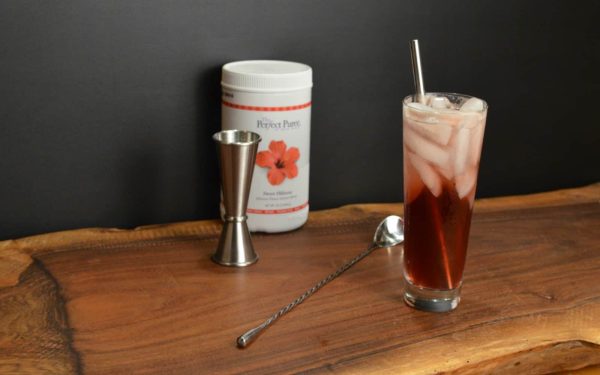 Amaretto hibiscus cocktail with barware and hibiscus powder beside it