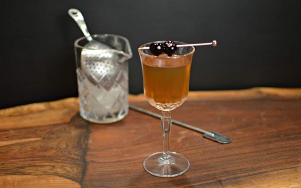 Remember the Maine cocktail with cocktail cherries, next to a mixing glass and julep strainer
