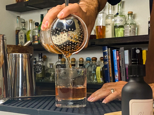 pouring a sazerac into a glass with absinthe, an anise-flavored liqueur