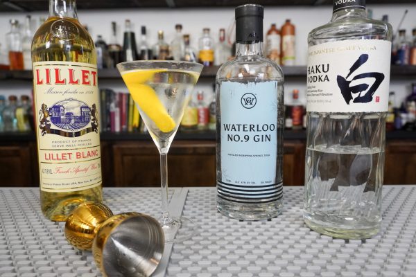 Vesper Martini surrounded by bottles of alcohol for the ingredients, plus a jigger from a cocktail kit