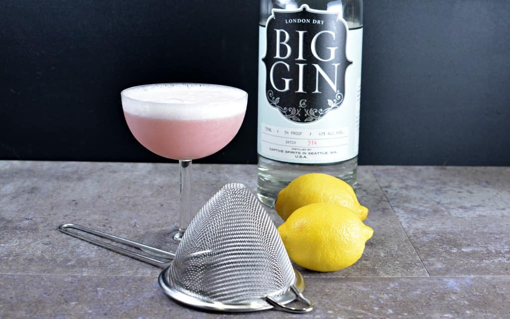 Clover Club cocktail with bottle of gin, fine strainer, and 2 lemons