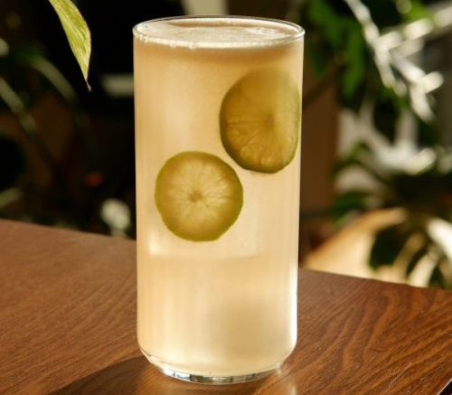 light yellow cocktail with lime slices in a Collins glass