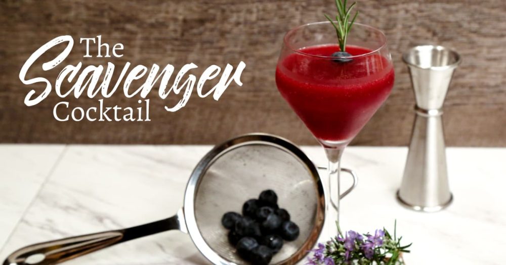 Scavenger drink, a red cocktail with blueberries and bar tools around it