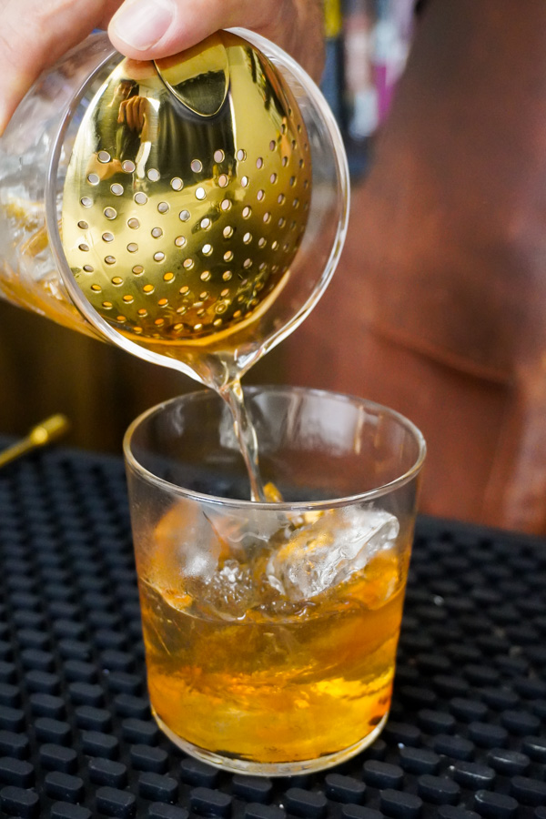 Pouring old fashioned with balanced flavor profiles into a whiskey glass from mixing glass