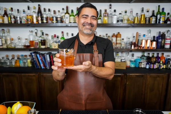 bartender holding cocktail with rye whiskey and a cocktail cherry and orange peel