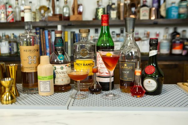 2 versions of 1 cocktail with their ingredients on a bar
