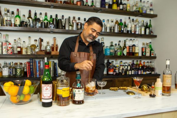 bartender stirring cocktail ingredients over ice with a bar spoon, in a mixing glass