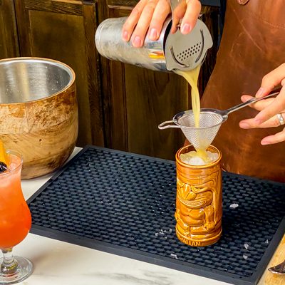 3. Pouring homemade Hurricane cocktail mix through a cocktail strainer into a tiki glass of choice