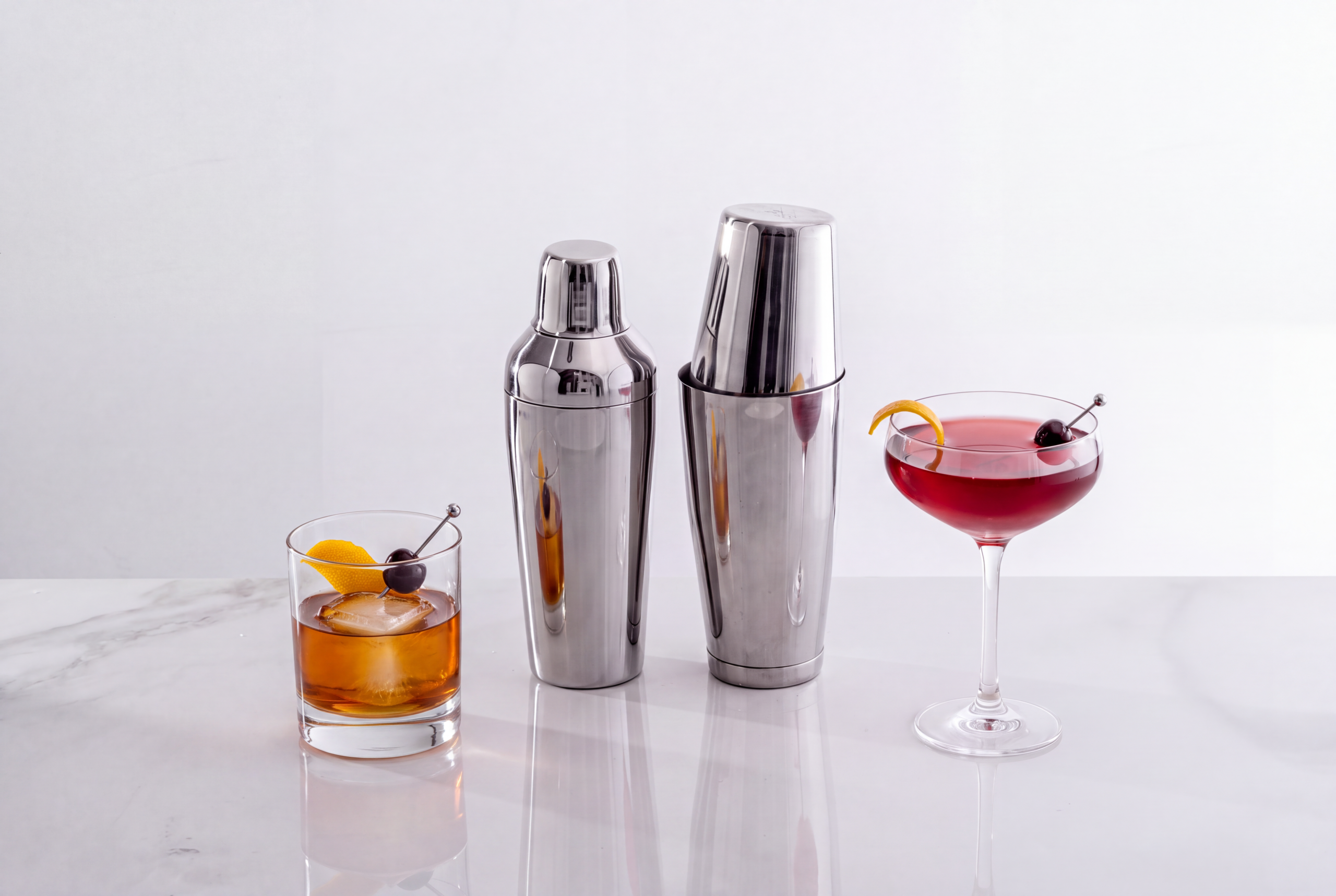 a cobbler shaker next to a Boston shaker, with a cocktail in a chilled coupe and an Old fashioned in a rocks glass