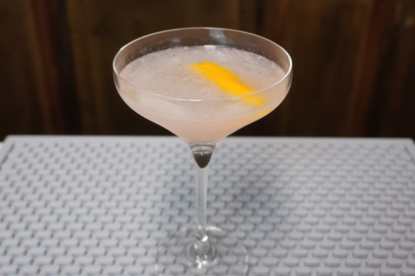 cosmopolitan drink in coupe cocktail glass large enough for a single martini with lemon twist