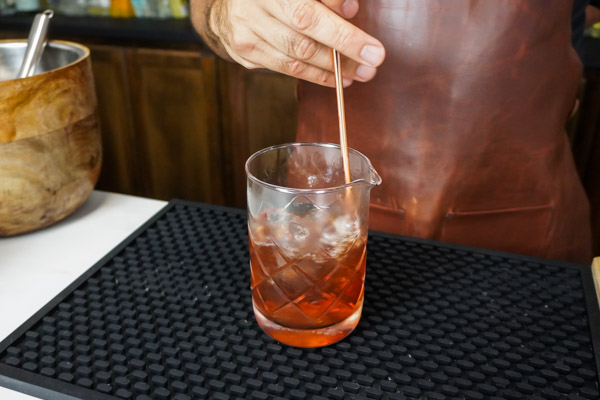 Stirring the Manhattan cocktail in a mixing glass before adding 2 dashes bitters