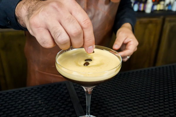 garnishing a martini glass with coffee beans on top of frothy foam