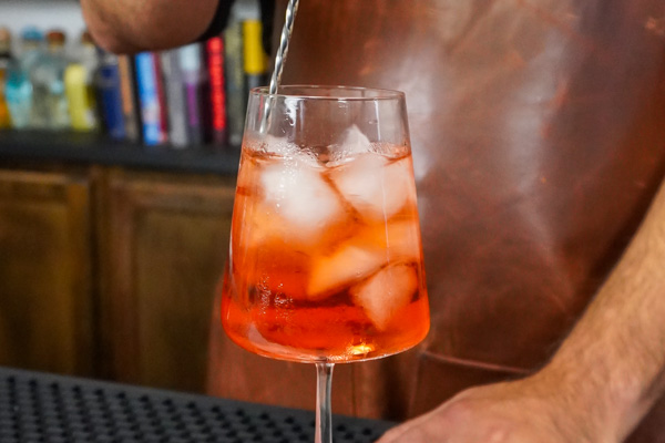 stirring a virgin aperol spritz with tart flavor and dark pink color