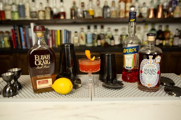 Paper Plane cocktail surrounded by its ingredients on a bar