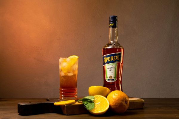 Bottle of Aperol with a drink in a highball glass with citrus fruit
