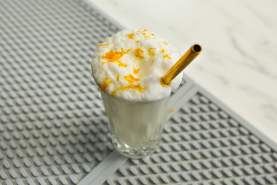 top down view of a ramos gin fizz cocktail with orange zest on top and a gold straw