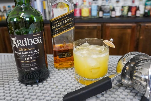 Penicillin drink with ginger root candy garnish on a bar with whisky, Scotch, and a lemon juicer,