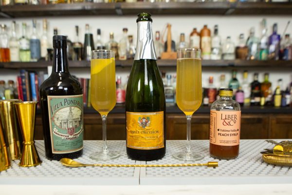 2 versions of the Bellini, surrounded with champagne and ingredients on a bar top