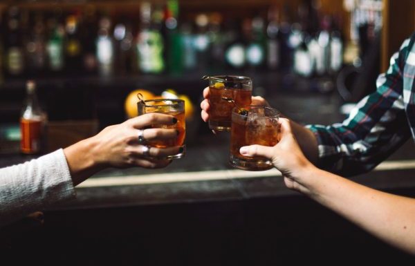 3 hands holding cocktails, clinking them together in a cheers, set in a bar