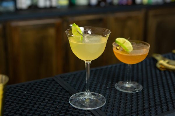 Variation of the Pegu Club, next to the original cocktail, both in coupe glasses on a bar