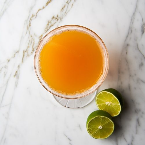 Pegu Club, a salmon pink cocktail, viewed from the top-down on a marble counter with 2 lime halves