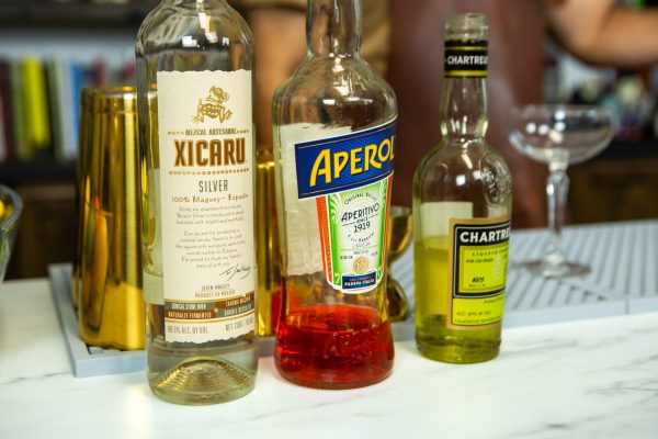 bottle of Mezcal, Aperol, and yellow Chartreuse on a bar