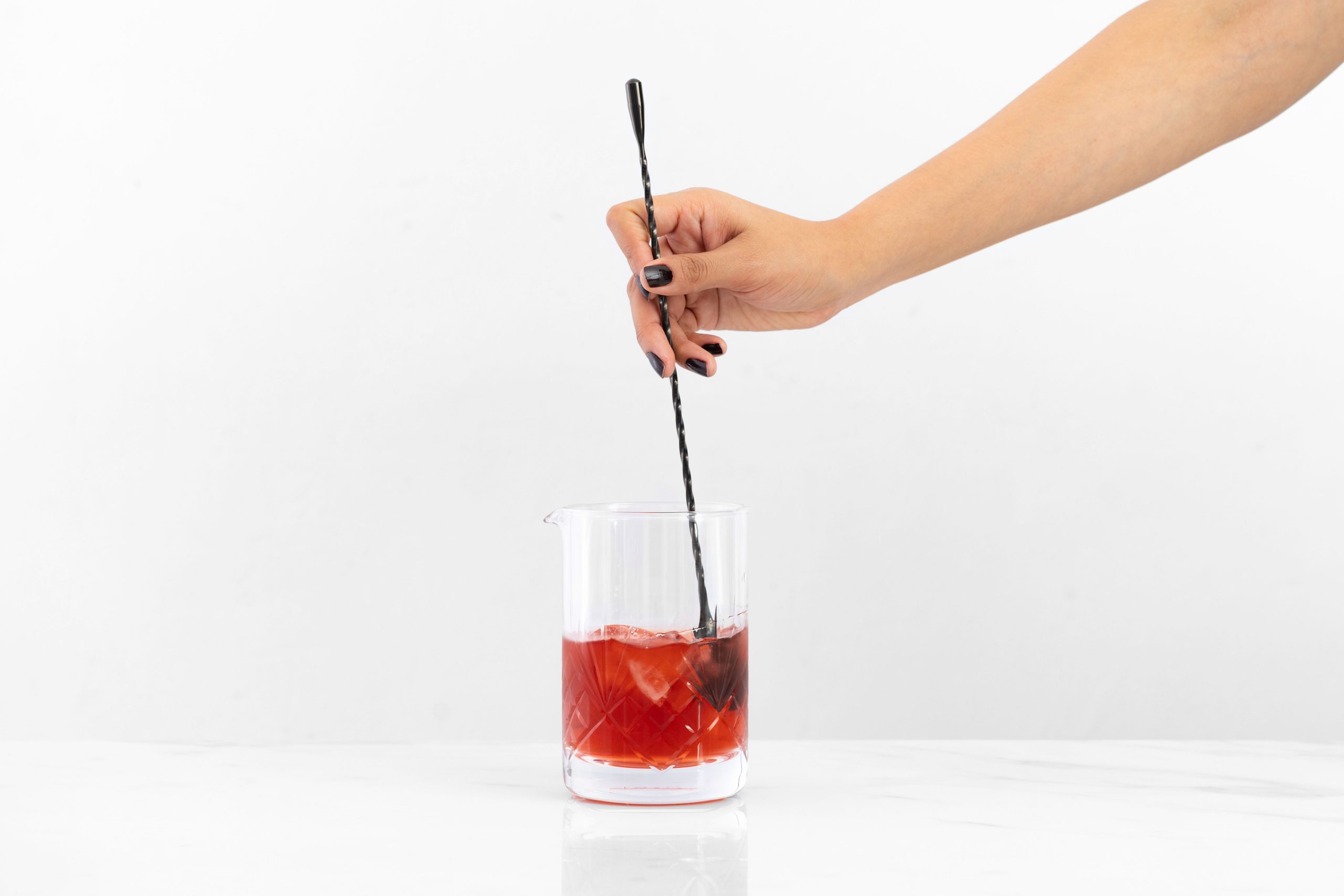 a hand mixing a drink in a mixing glass