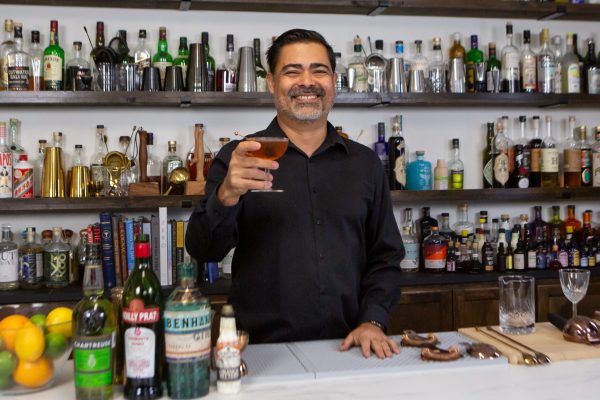 bartender holding up a cocktail and smiling in a bar