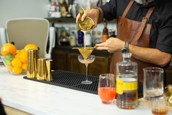 bartender's hand pouring a cocktail into a chilled coupe