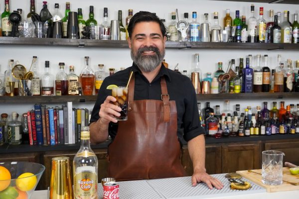 bartender holding an alcoholic drink made of Coca-Cola soda with a lime garnish, smiling in a bar