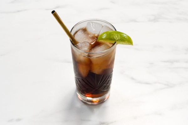 a conventional cola and rum cocktail with a gold straw and lime zest garnish
