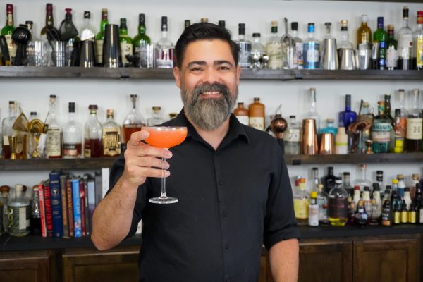 Bartending holding a drink in a chilled glass with orange slice garnish