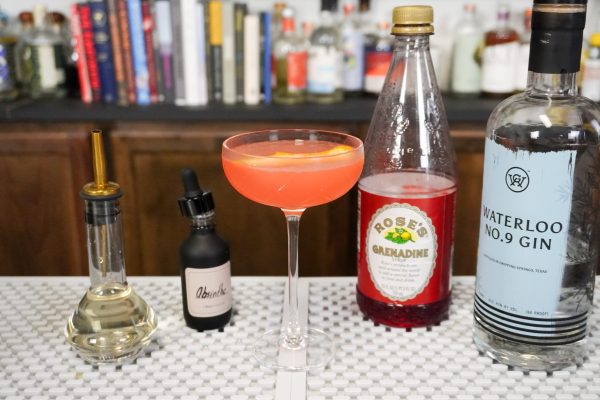 A citrusy cocktail surrounded by its ingredients on a bar