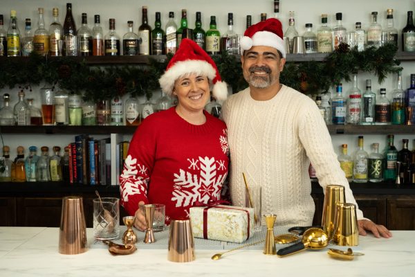 Chris and Julia Tunstall, the founders of A Bar Above, in their bar surrounded by barware and bar tool gifts for Christmas and the holidays, wearing Santa hats