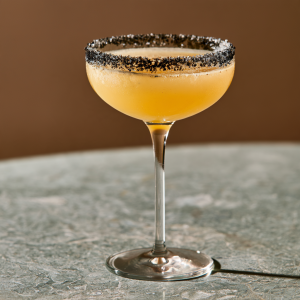 a yellow cocktail in a coupe glass with black salt rim