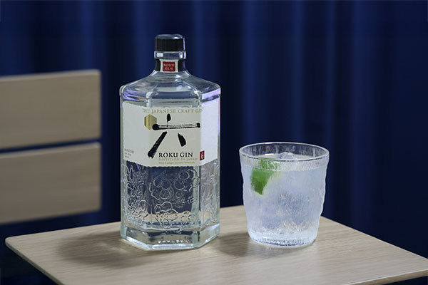 A bottle of gin, Roku gin, on a table next to a glass of Gin and Tonic