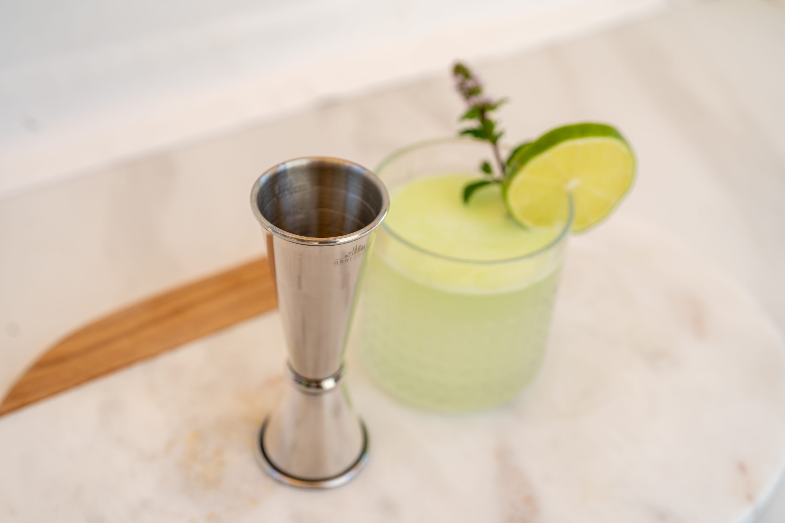 a silver Japanese jigger next to a Margarita in a rocks glass
