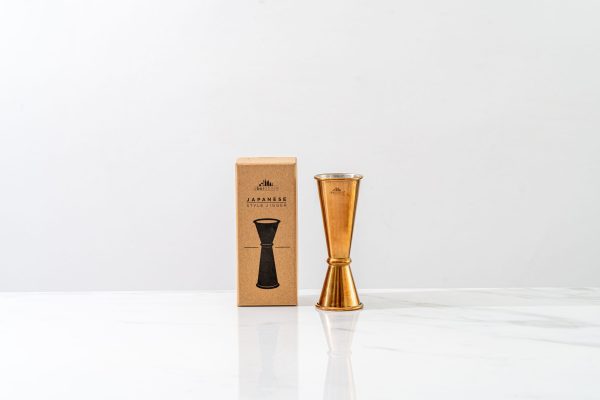 Gold cocktail jigger next to its box
