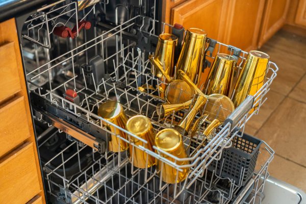 gold cocktail shakers, jiggers, and other barware in the top rack of a dishwasher