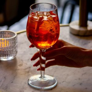 a hand holding a white wine glass full of aperitivo amaro with ice