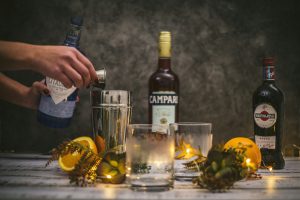 a hand pour cocktails with tea lights and oranges with a Campari bottle in the background