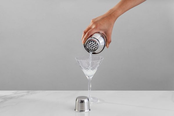 A cobbler shaker pouring a drink into a Martini glass