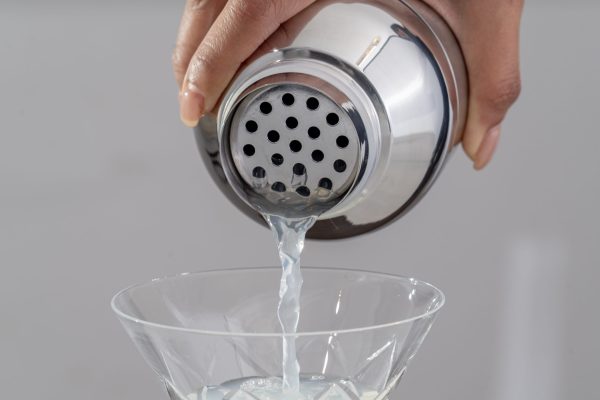 a close-up of a the top strainer attachment of a cobbler shaker, pouring a cocktail into a Martini glass