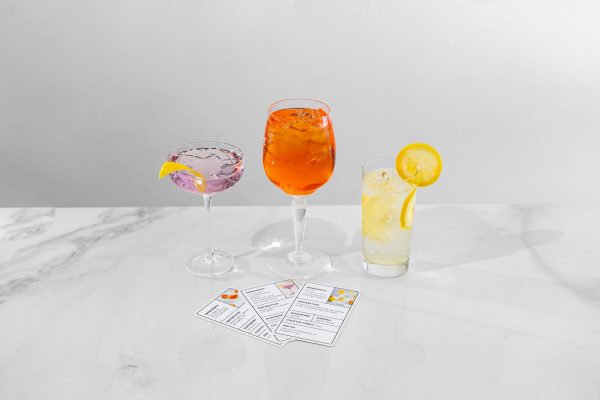 3 beautiful cocktails in different glasses, next to recipe cards